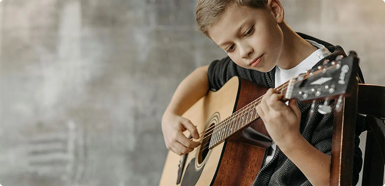 A young boy playing an acoustic guitar